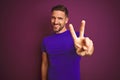 Young man wearing casual purple t-shirt over lilac isolated background smiling looking to the camera showing fingers doing victory Royalty Free Stock Photo