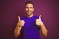 Young man wearing casual purple t-shirt over lilac isolated background success sign doing positive gesture with hand, thumbs up Royalty Free Stock Photo