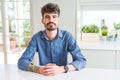 Young man wearing casual shirt sitting on white table Hands together and fingers crossed smiling relaxed and cheerful Royalty Free Stock Photo