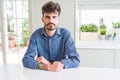 Young man wearing casual shirt sitting on white table skeptic and nervous, frowning upset because of problem Royalty Free Stock Photo