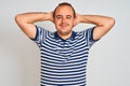 Young man wearing casual striped polo standing over isolated white background relaxing and stretching, arms and hands behind head Royalty Free Stock Photo