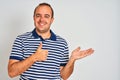 Young man wearing casual striped polo standing over isolated white background Showing palm hand and doing ok gesture with thumbs Royalty Free Stock Photo