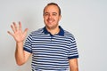 Young man wearing casual striped polo standing over isolated white background showing and pointing up with fingers number five