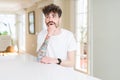 Young man wearing casual t-shirt sitting on white table with hand on chin thinking about question, pensive expression Royalty Free Stock Photo