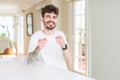 Young man wearing casual t-shirt sitting on white table pointing fingers to camera with happy and funny face Royalty Free Stock Photo