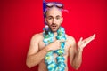 Young man wearing diving snorkel goggles and hawaiian lei flowers over isolated red background amazed and smiling to the camera