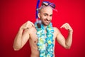 Young man wearing diving snorkel goggles and hawaiian lei flowers over isolated red background looking confident with smile on