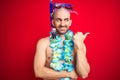 Young man wearing diving snorkel goggles and hawaiian lei flowers over isolated red background smiling with happy face looking and