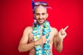 Young man wearing diving snorkel goggles and hawaiian lei flowers over isolated red background smiling and looking at the camera