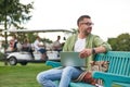 Young man wearing eyeglasses looking away while working using laptop, sitting on the bench in the green park Royalty Free Stock Photo