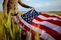 Young man wearing green shirt and cap lets the american flag fly on the wind at the green wheat field. Patriotic boy celebrates Royalty Free Stock Photo