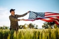 Young man wearing green shirt and cap lets the american flag fly on the wind at the green wheat field. Patriotic boy celebrates Royalty Free Stock Photo