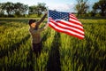 Young man wearing green shirt and cap lets the american flag fly on the wind at the green wheat field. Patriotic boy celebrates Royalty Free Stock Photo