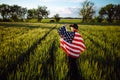 Young man wearing green shirt and cap stands wrapped in the american flag at the green wheat field. Patriotic boy celebrates usa Royalty Free Stock Photo