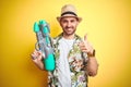Young man wearing hawaiian flowers shirt holding water gun over yellow isolated background happy with big smile doing ok sign, Royalty Free Stock Photo