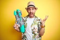 Young man wearing hawaiian flowers shirt holding water gun over yellow isolated background very happy and excited, winner Royalty Free Stock Photo