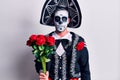 Young man wearing mexican day of the dead costume holding flowers thinking attitude and sober expression looking self confident
