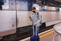 Young man wearing protective face mask standing on the railway station near the train. Royalty Free Stock Photo