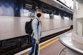 Young man wearing protective face mask standing on the railway station near the train. Royalty Free Stock Photo