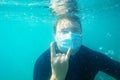 Young man wearing protective medical mask on face and smart watch on wrist is diving, swimming under water. New Royalty Free Stock Photo