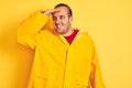 Young man wearing rain coat standing over isolated yellow background very happy and smiling looking far away with hand over head Royalty Free Stock Photo