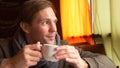 Young Man Wearing a Scarf Drinking Tea and Smiling in a cafe.