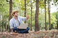 A young man wearing a straw hat happily uses a notebook while working in the forest garden.