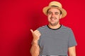 Young man wearing striped navy t-shirt and hat standing over isolated red background smiling with happy face looking and pointing Royalty Free Stock Photo
