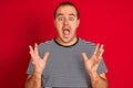 Young man wearing striped navy t-shirt standing over isolated red background celebrating crazy and amazed for success with arms Royalty Free Stock Photo