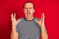 Young man wearing striped navy t-shirt standing over isolated red background celebrating mad and crazy for success with arms Royalty Free Stock Photo