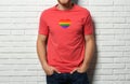 Young man wearing t-shirt with image of heart shaped LGBT pride flag near white brick wall Royalty Free Stock Photo