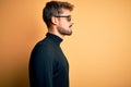 Young man wearing thug life fanny sunglasses standing over isolated yellow background looking to side, relax profile pose with Royalty Free Stock Photo