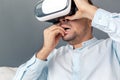 Freestyle. Young man in virtual reality headset studio sitting on sofa isolated on grey playing biting nails nervous Royalty Free Stock Photo