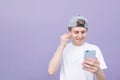 Young man wearing a white T-shirt listens to music in headphones and uses a smartphone on a purple pastel background Royalty Free Stock Photo