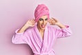 Young man wearing woman make up wearing shower towel on head and bathrobe smiling pulling ears with fingers, funny gesture Royalty Free Stock Photo