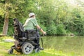 Happy man in a electric wheelchair throwing fishing pole at the beautiful pond in natue on a sunny day