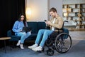 Young man in wheelchair holding mobile phone in hands and his wife using laptop at home Royalty Free Stock Photo
