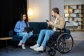 Young man in wheelchair holding mobile phone in hands and his wife using laptop at home Royalty Free Stock Photo