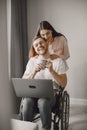 Young man in wheelchair using laptop and girlfriend hugging him at home