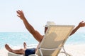 Young man in white hat relaxing in deck chair on beautiful sandy beach Royalty Free Stock Photo