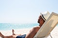 Young man in white hat relaxing in deck chair on beautiful sandy beach Royalty Free Stock Photo