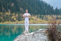 A young man in white practices yoga in the mountains lake. Pose Samasthiti namaskar Royalty Free Stock Photo