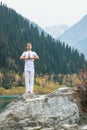 A young man in white practices yoga in the mountains. Pose Samasthiti namaskar Royalty Free Stock Photo