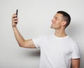 Young man in white shirt holding mobile phone and making photo of himself