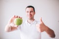 Young man in white shirt isolated over background. Guy hold green apple in hand and smile. Show big thumb up. Yummy Royalty Free Stock Photo