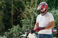 Young man in white shirt and jeans putting on his gloves near a motorcycle outdoors