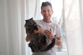 Young man in the white shirt and pajama is smiling holding fluffy cat which wants to run away Royalty Free Stock Photo