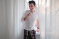 Young man in the white shirt and pajama is smiling relaxing lsitting on a window sill. Royalty Free Stock Photo