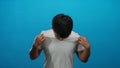 Young man in white shirt stands against isolated blue background looking down with a contemplative expression, capturing Royalty Free Stock Photo