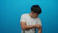 Young man in white shirt stands against isolated blue background looking down with a contemplative expression, capturing Royalty Free Stock Photo